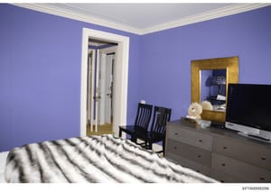 This is a photograph of a bedroom interior, likely from a property belonging to Jeffrey Epstein or associated with the investigation. The room features distinctive purple walls, modern furniture, and various personal items. The image appears to be ev
