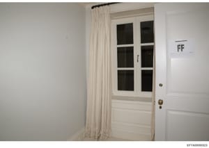 This is an evidence photograph showing the interior of a room with a white wooden door featuring six glass panes, white walls, and cream-colored curtains. The image appears to be from a property inspection or evidence documentation related to the inv