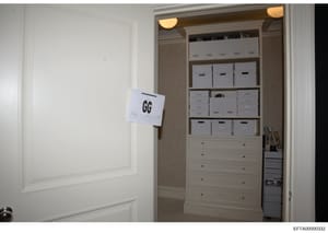 This is an evidence photograph from an Epstein property search showing a walk-in closet containing multiple white storage boxes organized on shelving units, with a lower section featuring drawers. An evidence marker labeled 'GG' is visible on the lef