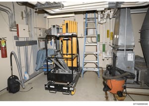 This is a photograph of a basement utility room, likely from one of Jeffrey Epstein's properties, showing mechanical systems including HVAC equipment, electrical panels, ladders, tools, and various maintenance equipment. The image documents the infra