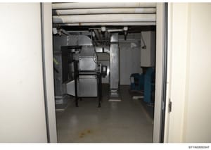 This photograph shows an interior mechanical or equipment room, likely in a basement or utility area of a building. The room contains industrial HVAC equipment, metal ductwork, electrical panels, and various mechanical systems. The image appears to b