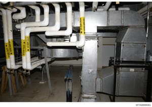 This is an evidence photograph showing HVAC piping, ductwork, and mechanical systems in what appears to be a basement or utility area of a property. Multiple white PVC pipes with yellow evidence tags are visible, suggesting this area was photographed