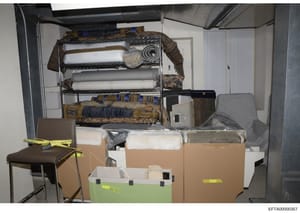 This is a photographic record of a storage or evidence room containing confiscated items seized during the investigation. The image shows a metal shelving unit with rolled materials, fabrics, and patterned textiles, along with cardboard boxes and a b