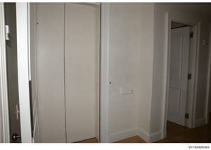 This is an evidence photograph showing the interior of a residential room with white walls, closet doors, and hardwood flooring. The image appears to be documentation of a property space, likely from the Jeffrey Epstein investigation. The room is spa