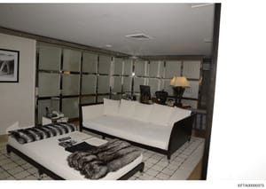 This photograph shows a contemporary bedroom interior with minimalist design, featuring two white platform beds with black frames, an elaborate built-in headboard wall system with frosted glass panels, and modern décor. The image appears to be eviden