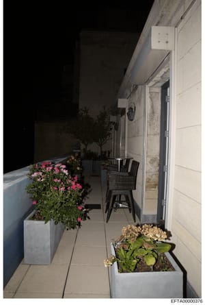 This photograph shows an outdoor terrace or balcony area featuring modern architectural elements, decorative planters with pink flowers and dried hydrangeas, black wicker seating, and stone/tile flooring. The image appears to be documentation of a pr