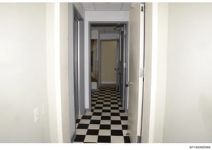 This is a photograph of an interior hallway, likely from one of Jeffrey Epstein's properties, showing a long corridor with black and white checkered tile flooring, white walls, and multiple doorways. The image appears to be part of the property docum