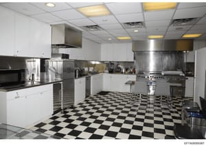 This is a photograph of a large, commercial-style kitchen with high-end appliances and finishes. The kitchen features white cabinetry, stainless steel professional-grade equipment, checkered black-and-white flooring, and recessed ceiling lights. This
