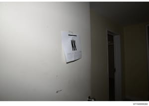 This is an evidence photograph showing the interior of a room with a wall-mounted thermostat unit and an adjacent doorway. The image appears to be part of a property documentation or forensic investigation record, with minimal markings or identifying