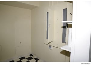 This is a photograph of an interior room in what appears to be under construction or renovation. The space features cream-colored drywall, dark-framed doorways or openings, a white shelf or ledge on the right side, and a distinctive black and white c
