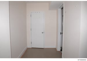 This is an evidence photograph showing an interior room space, likely part of a property inspection or documentation. The room appears empty with white drywall, a white closet door in the center, and an open doorway to the right leading to another sp