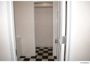 This is a photograph of an interior hallway or corridor featuring a distinctive black and white checkered floor pattern. The image shows white painted walls, framed doorways, and minimal furnishings. The photo appears to be documentation of a propert