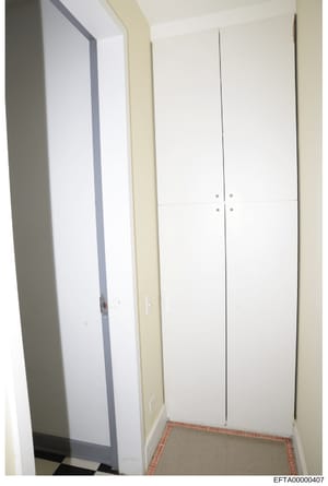 This is a photograph of an interior hallway or passage showing two white double doors with silver hardware, cream-colored walls, and a red/orange tile floor border. The image appears to be evidence documentation from a property inspection, likely fro