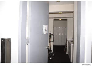 This photograph depicts an interior hallway or corridor space, showing built-in storage lockers, a light switch panel, recessed ceiling lighting, and a hand truck or dolly positioned in the passageway. The image appears to be part of property documen