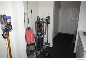 This is an evidence photograph showing the interior of a utility closet containing various cleaning equipment including commercial vacuum cleaners, mops, brooms, and cleaning supplies. The image documents the maintenance and housekeeping facilities a