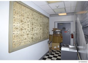 This photograph shows a small interior room or storage space, likely part of a building under investigation. The room contains cardboard boxes labeled 'Barrel' and other storage items, with a decorative framed wall panel featuring traditional Asian-i