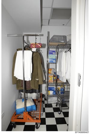 This is a photograph of a storage or utility room, likely from an Epstein residence, showing metal clothing racks, linens, household goods, and various packaged items on shelves. The image documents the interior of a storage space with organized supp