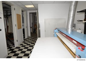 This is an evidence photograph showing an interior space with a black-and-white checkered floor, multiple doorways, storage areas, and what appears to be commercial or institutional equipment including a large blue counter or table on the right side.