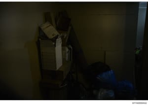 This is an evidence photograph showing stacked cardboard boxes and files in what appears to be a storage or evidence facility. The image is poorly lit and taken at an angle, making specific details difficult to discern. The photograph is part of the 