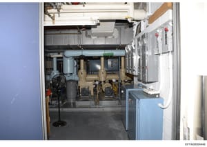 This is a photograph of a mechanical/utility room showing building infrastructure including HVAC equipment, pumps, piping systems, electrical panels, and other mechanical systems. The image appears to be from a property inspection or inventory docume