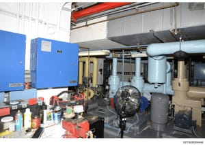 This photograph shows an industrial mechanical or utility room containing HVAC and building systems infrastructure. The image depicts a Siemens blue control panel, piping systems, fans, and various mechanical equipment in what appears to be a commerc
