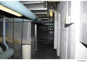 This is an evidence photograph showing an interior basement or mechanical space containing HVAC piping, ductwork, electrical systems, and various mechanical equipment. The image appears to be part of a property inspection or forensic documentation, w