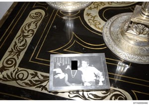 This is an evidence photograph showing a black-and-white photograph placed on an ornate black surface with gold inlay designs and decorative silver objects. The photograph within the image shows three people in what appears to be an indoor setting, w