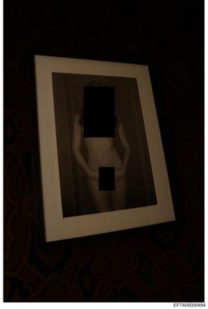 This is an evidence photograph showing a framed portrait with the subject's face and lower body pixelated/redacted for privacy protection. The image appears to be taken in low lighting conditions and shows the frame mounted or displayed against a dar