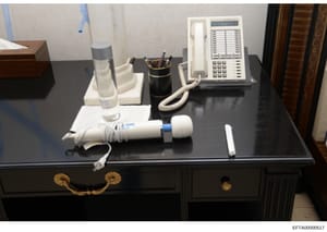 Evidence photograph documenting a desk setup within an Epstein property, showing office furnishings and equipment including a multi-line telephone system, water glass, pen holder, and other desk accessories. This appears to be documentation of interi