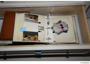 This is a photograph of a three-ring binder containing a collection of photographs and images, many of which have been redacted with black boxes by investigators. The binder appears to have been seized as evidence and is shown on a shelf in what appe