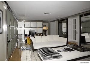 This photograph shows a luxurious bedroom interior featuring modern furnishings and design elements. The space includes a large white upholstered sofa, a bed with striped bedding, multiple storage solutions with white cabinetry, a desk area with comp