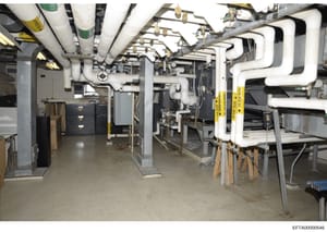 This photograph documents a basement or utility room showing extensive HVAC ductwork, plumbing systems, and mechanical equipment. The image appears to be an interior inspection or documentation photo of building infrastructure, likely from one of Eps