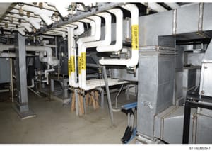 This photograph shows an interior view of a basement or mechanical room containing heating, ventilation, and air conditioning (HVAC) equipment along with extensive white PVC piping systems. The image appears to be documentation of building infrastruc
