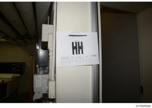 This is an evidence photograph showing a document with 'HH' branding posted on what appears to be an interior wall or door frame. The document contains a table with columns for tracking information (Search Personnel Name, Agency, Contact Number, Init