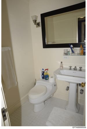 This is a photograph of a residential bathroom, likely from one of Jeffrey Epstein's properties. The image shows a standard bathroom with toilet, sink, mirror, and vanity, documented as part of the investigative evidence collection. The bathroom appe