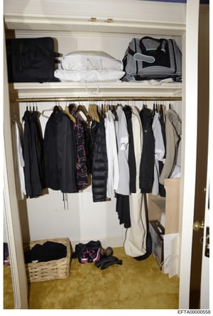 This is an evidence photograph showing the interior of a residential closet containing various clothing items, luggage, and personal belongings. The closet displays an organized collection of garments on hangers along with packed suitcases and storag