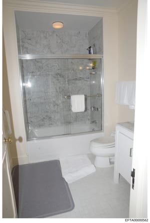 This is a color photograph of a residential bathroom showing a glass-enclosed shower with marble tile walls, white porcelain fixtures, and contemporary finishes. The image appears to be documentation of property interior conditions, likely taken duri