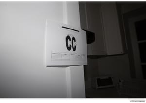 This is an evidence photograph taken during the investigation showing an interior doorway or wall area marked with a large 'GG' reference label and an accompanying search log sheet. The marker and documentation sheet are standard forensic photography