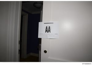 This is an evidence photograph showing an interior doorway with a white evidence marker labeled 'AA' attached to the door frame. The photo documents a room entrance with white trim, ceiling fixture, and brass doorknob. This type of documentation is s