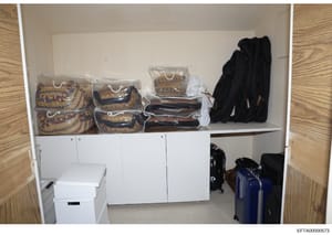 This is a photograph of a walk-in closet or storage area containing organized shelving with packaged decorative items, clothing, and luggage. The image shows multiple clear plastic storage bags containing patterned textiles or decorative goods in gol