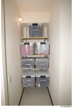 Evidence photograph showing an interior storage closet containing multiple clear plastic storage containers organized on wall-mounted shelving. The containers appear to hold various items including folded materials in pink and white packaging. This p