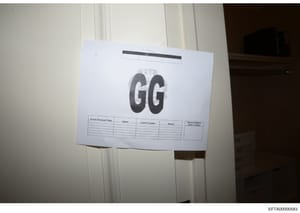 This is an evidence photograph showing a document or form affixed to a wall or surface, labeled with the initials 'GG' and containing a table with column headers for 'Search Personnel Name,' 'Agency,' 'Contact Number,' 'Initials,' and 'Search Complet