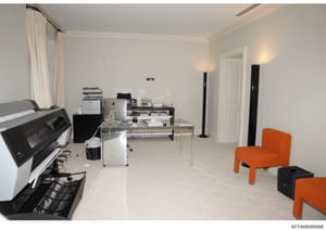 This is a photograph of a modern office space, likely part of an Epstein property, showing a well-furnished workspace with contemporary furniture, office equipment including printers and multifunction devices, and distinctive orange accent chairs. Th