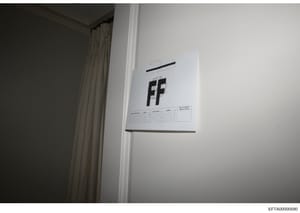 This is an evidence photograph showing a document or evidence marker labeled 'FF' affixed to an interior wall, likely taken during a property search or forensic documentation. The marker includes a reference grid and appears to be standard law enforc