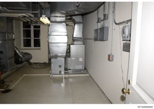 This photograph shows a basement mechanical room containing heating, ventilation, and air conditioning (HVAC) equipment, electrical panels, and utility infrastructure. The image captures the infrastructure of a residential property, likely from one o