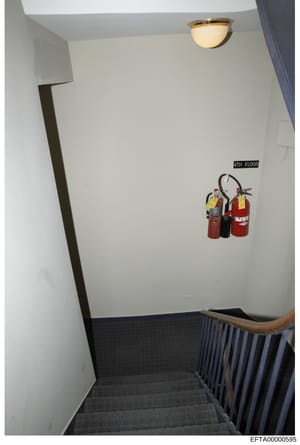 This is an evidence photograph of a stairwell on the 4th floor of a property, showing basic interior features including fire extinguishers mounted on the wall, ceiling fixtures, and building infrastructure. The photo appears to be part of a property 