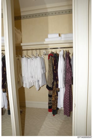 This is a photograph of a walk-in closet interior showing organized clothing storage, including white garments, decorative patterned robes or wraps with gold embroidery, and folded linens on upper shelves. The closet appears to be in a residential pr