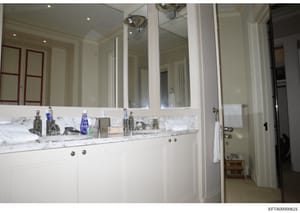 This is a photograph of an upscale bathroom interior, likely from one of Jeffrey Epstein's properties, showing a double vanity setup with marble countertop, large mirrored wall cabinet, and various personal items. The image documents the interior des