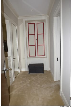 This is an evidence photograph depicting an interior hallway of a residential property, featuring white painted walls, recessed ceiling lighting, multiple white panel doors on either side, and a distinctive white door with red geometric frame pattern