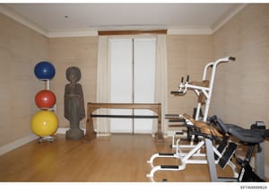 This photograph shows an interior gymnasium or fitness room in what appears to be one of Jeffrey Epstein's residences. The room contains multiple pieces of exercise equipment including stationary bicycles, exercise balls, and weight machines, along w